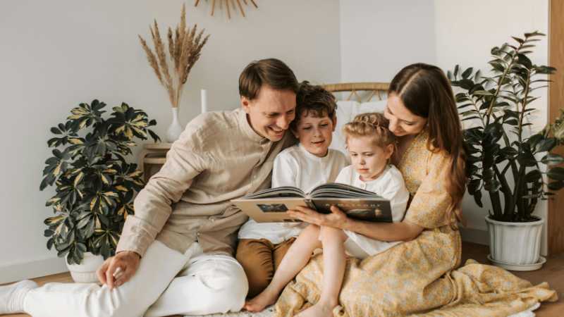 Happy family sitting together on floor, enjoying a book in cozy home environment., tags: und - pexel